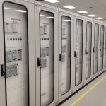 Sala de controle industrial com fileiras de painéis elétricos iluminados