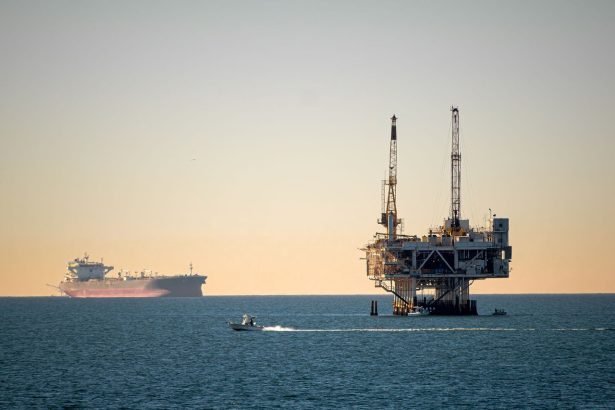 Plataforma de petróleo offshore no mar, com um navio porta-contêineres ao lado durante o dia.