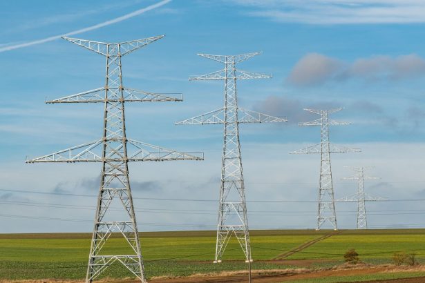 Torres de transmissão de energia elétrica se estendem por campos verdes sob céu azul.