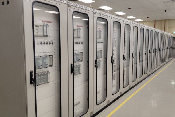 Sala de controle industrial com fileiras de painéis elétricos iluminados
