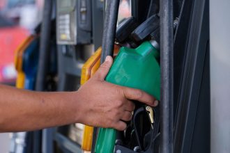 Mão segurando um bico verde de abastecimento em um posto de combustíveis
