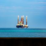 Plataforma de petróleo offshore ao longe, cercada pelo oceano sob céu claro.