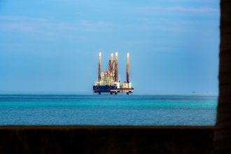 Plataforma de petróleo offshore ao longe, cercada pelo oceano sob céu claro.