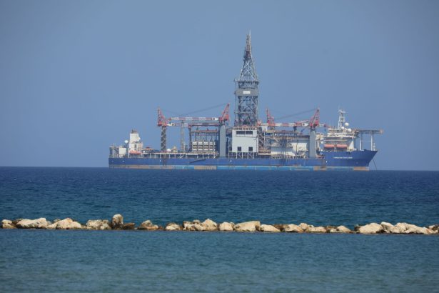 Sonda de perfuração de petróleo flutuando em mar aberto sob céu azul.